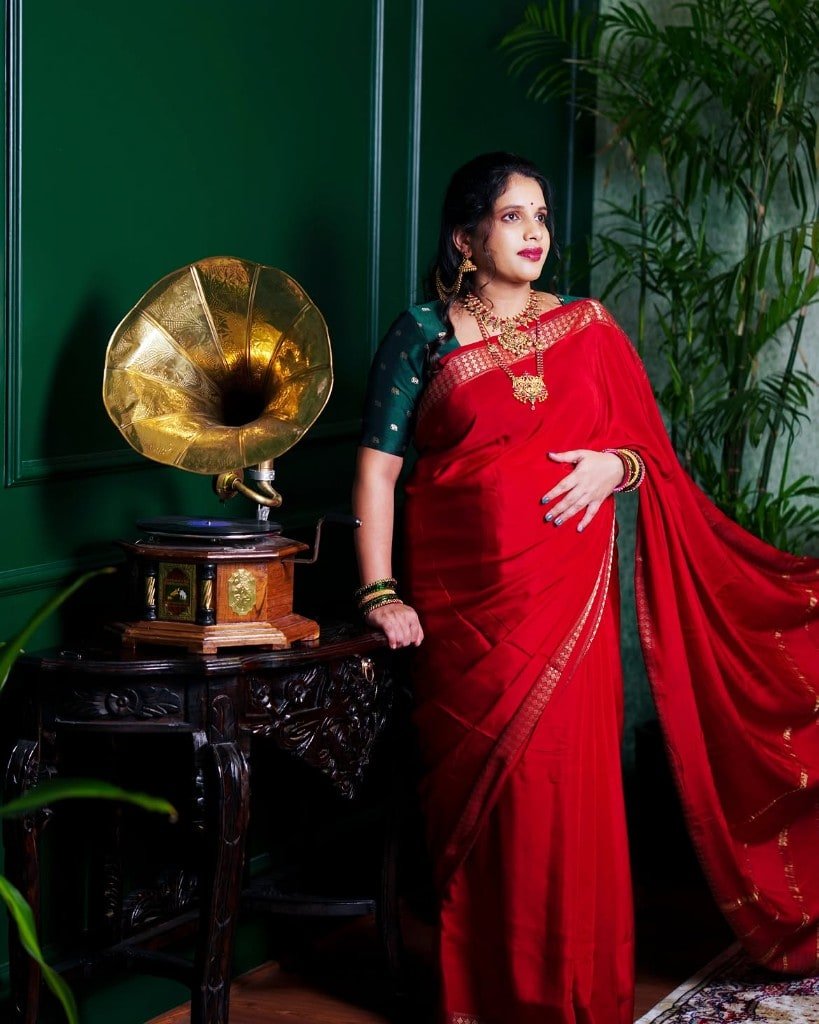 Maternity portrait in a red saree, holding the bump